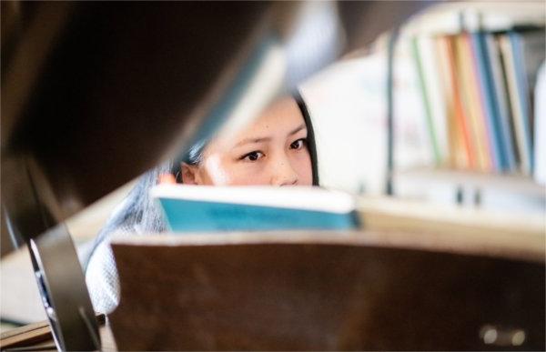 A person seen through the opened top of a baby grand piano peers at a music book.